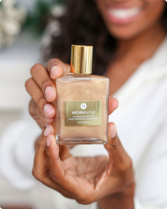 Woman smiling and holding Neora’s hottest holiday limited-time must-have, Glisten Up Holiday Body Glow Oil. 
