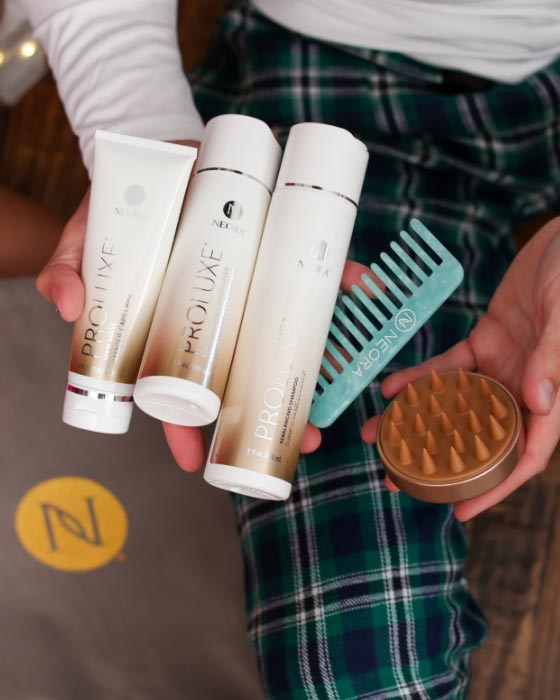 Man holding Neora’s hottest holiday must-have, the Get-Gorgeous Holiday Hair Set, which includes ProLuxe™ Rebalancing Shampoo, ProLuxe™ Rebalancing Conditioner, ProLuxe™ Hair Mask, FREE Detangling Comb + FREE Scalp Scrubber and FREE Gift Bag.  